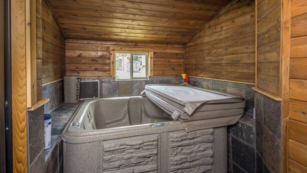 Interior de una cabaña de madera con baño de baldosas de piedra, una ventana y un perchero.