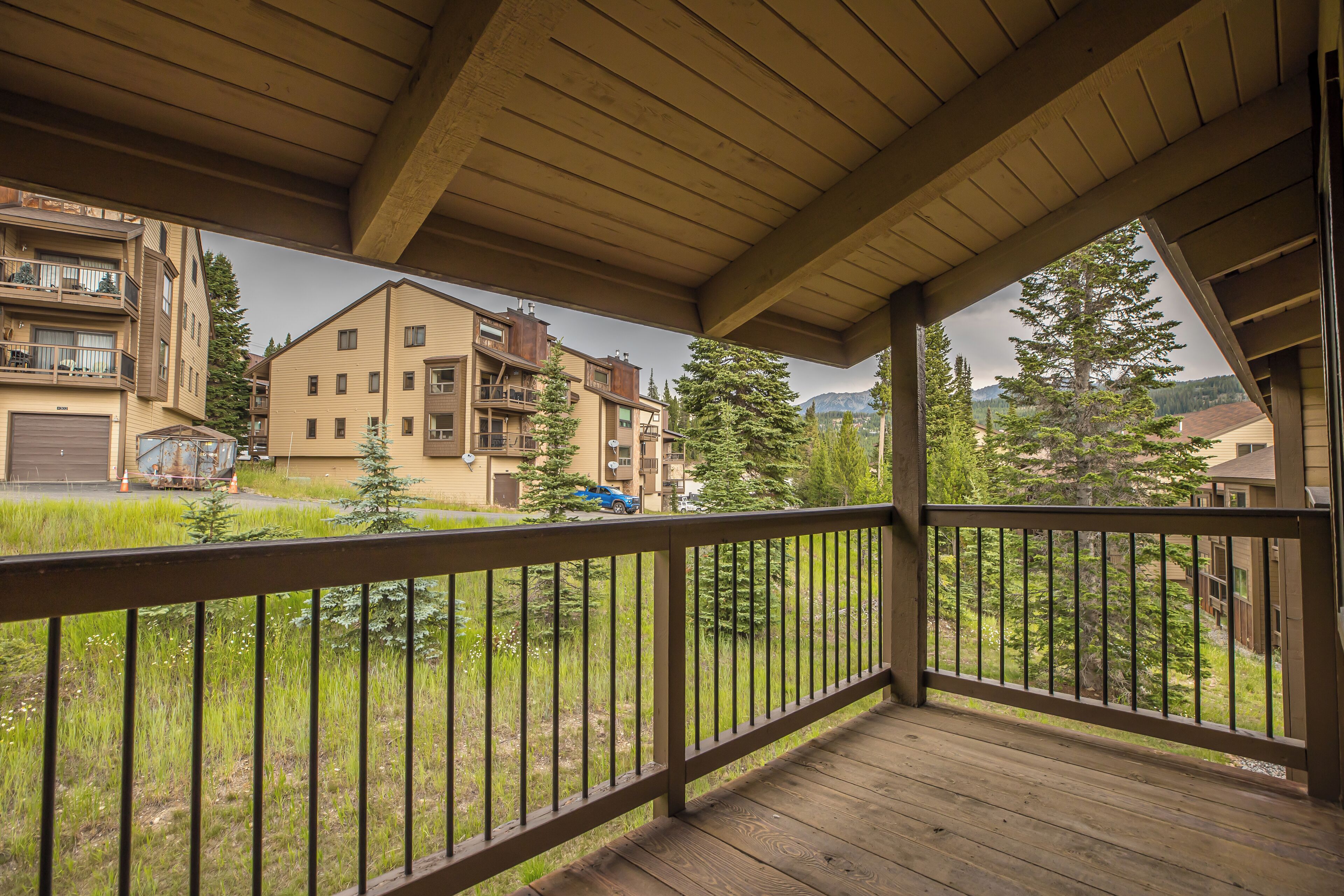 A wooden balcony with a metal railing overlooking a residential area with houses and trees.