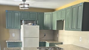 A kitchen with green cabinets, a granite countertop, and three black stools. - 1800 Historic Studio in  downtown Dunnellon Rainbow River World Equestrian ctr (Dunnellon)