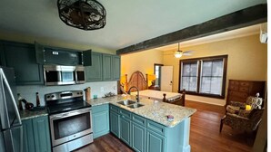 A kitchen with teal cabinets, stainless steel appliances, a granite countertop, and a wooden island with a sink. - 1800 Historic Studio in  downtown Dunnellon Rainbow River World Equestrian ctr (Dunnellon)