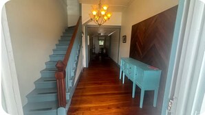 A staircase with wooden steps and a handrail, leading to a hallway with a chandelier and a blue bench. - 1800 Historic Studio in  downtown Dunnellon Rainbow River World Equestrian ctr (Dunnellon)