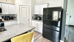 A modern kitchen with a granite countertop, stainless steel appliances, and a yellow chair.