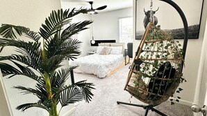 A modern bedroom with a bed, a hanging chair with plants, and a large potted plant.