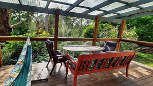 A wooden deck with a bench and chairs, surrounded by lush greenery and a view of trees and plants.