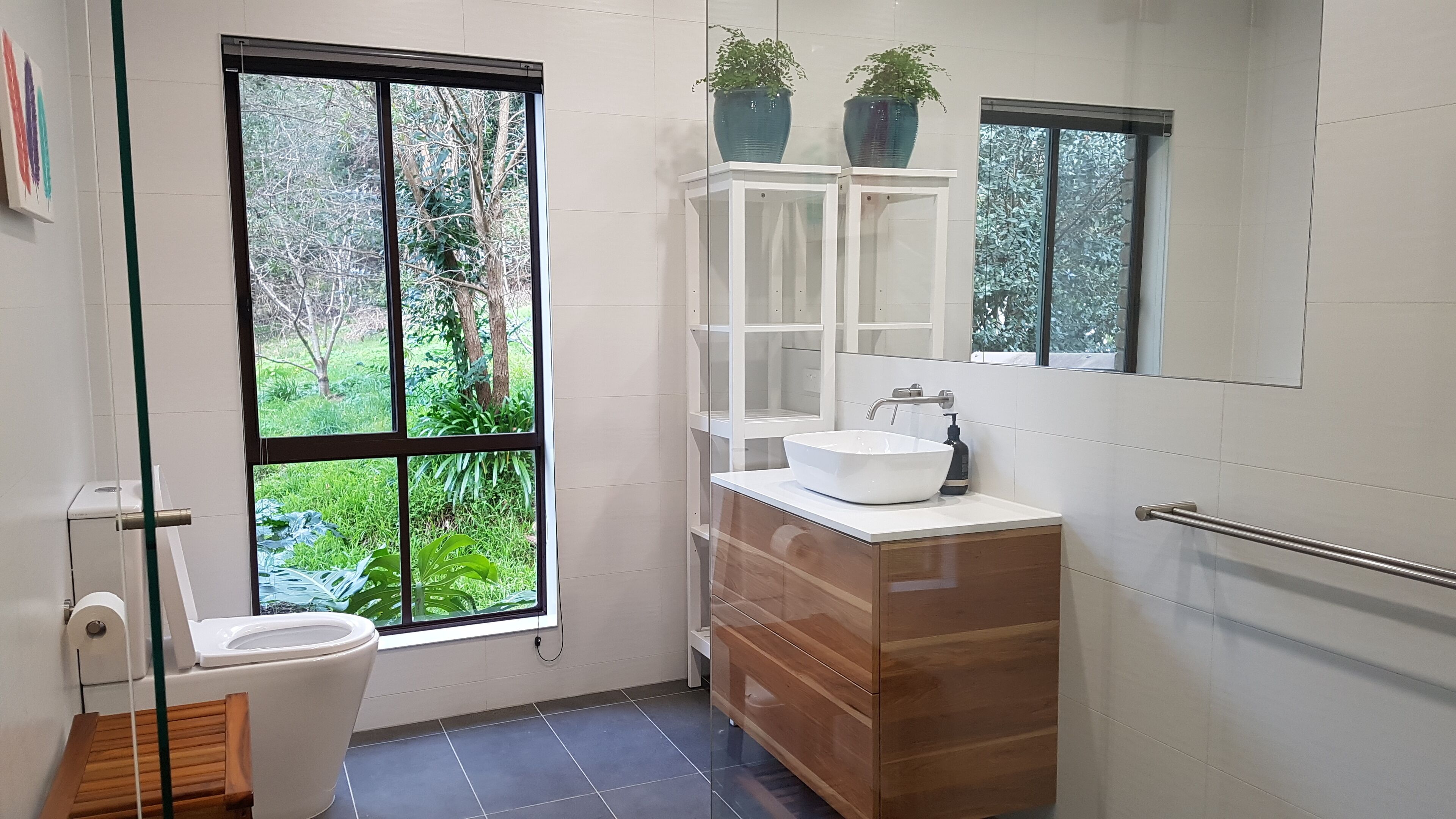 A modern bathroom with a large window, a white sink, and a wooden vanity.