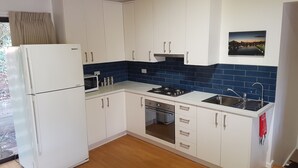 A compact kitchen with white cabinets, a white refrigerator, a gas stove, and a sink.