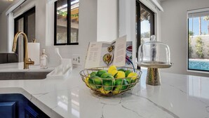 A modern kitchen with a marble countertop, a gold faucet, a fruit bowl, and a view of the outdoors. - Azure Oasis - Saltwater Pool/Spa with putting green! (Palm Desert)