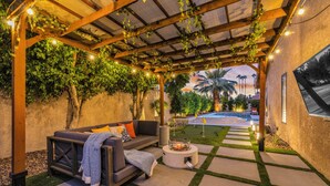 An outdoor patio with a wooden pergola, a sofa, and a fire pit. - Azure Oasis - Saltwater Pool/Spa with putting green! (Palm Desert)