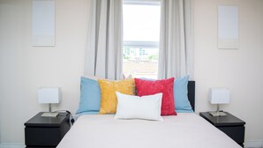Een slaapkamer met een bed, twee nachtkastjes en een raam met gordijnen.