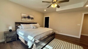 A bedroom with a bed, nightstands, a ceiling fan, a patterned rug, and a door.