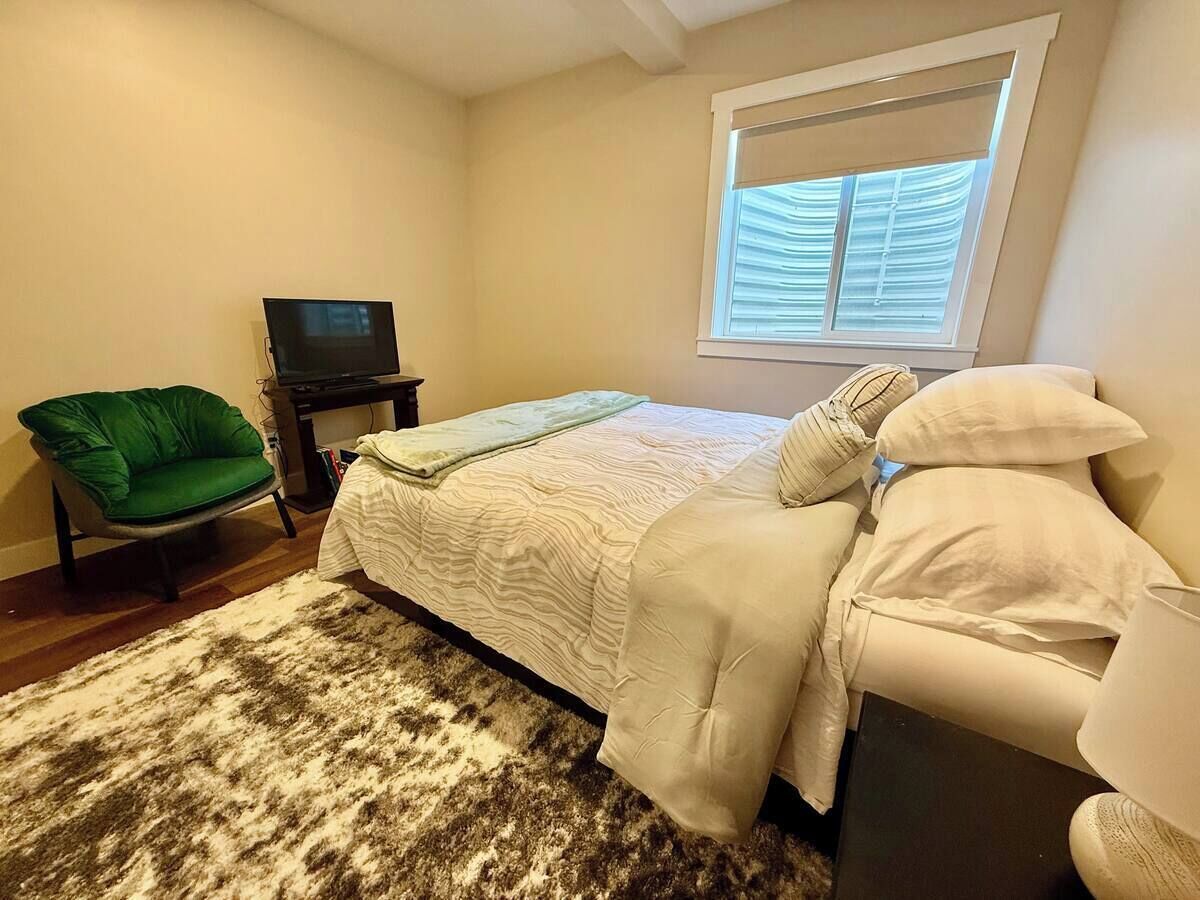 Une chambre à coucher avec un lit, un fauteuil vert, une télévision et une fenêtre avec des stores.