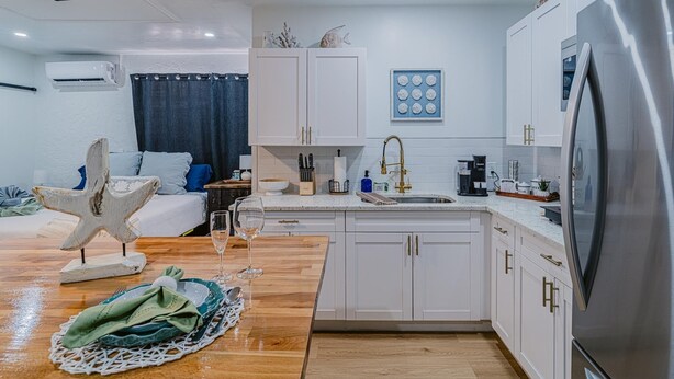 A modern kitchen with white cabinets, a stainless steel refrigerator, and a wooden dining table set with a starfish decoration and a glass of wine. - Charming studio in tranquil Naples with AC. (Naples)
