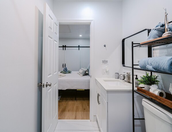 A compact, modern bathroom with a white sink, a mirror, and a shelf with towels.
