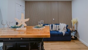 A modern living room with a wooden dining table, blue sofa, and a striped wall panel. - Charming studio in tranquil Naples with AC. (Naples)