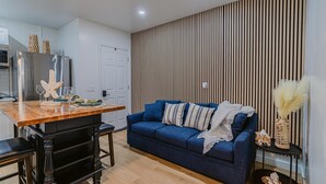 A modern kitchen with a built-in fridge, wooden dining table, and bar stools. A blue sofa with patterned cushions is against a striped wall. - Charming studio in tranquil Naples with AC. (Naples)