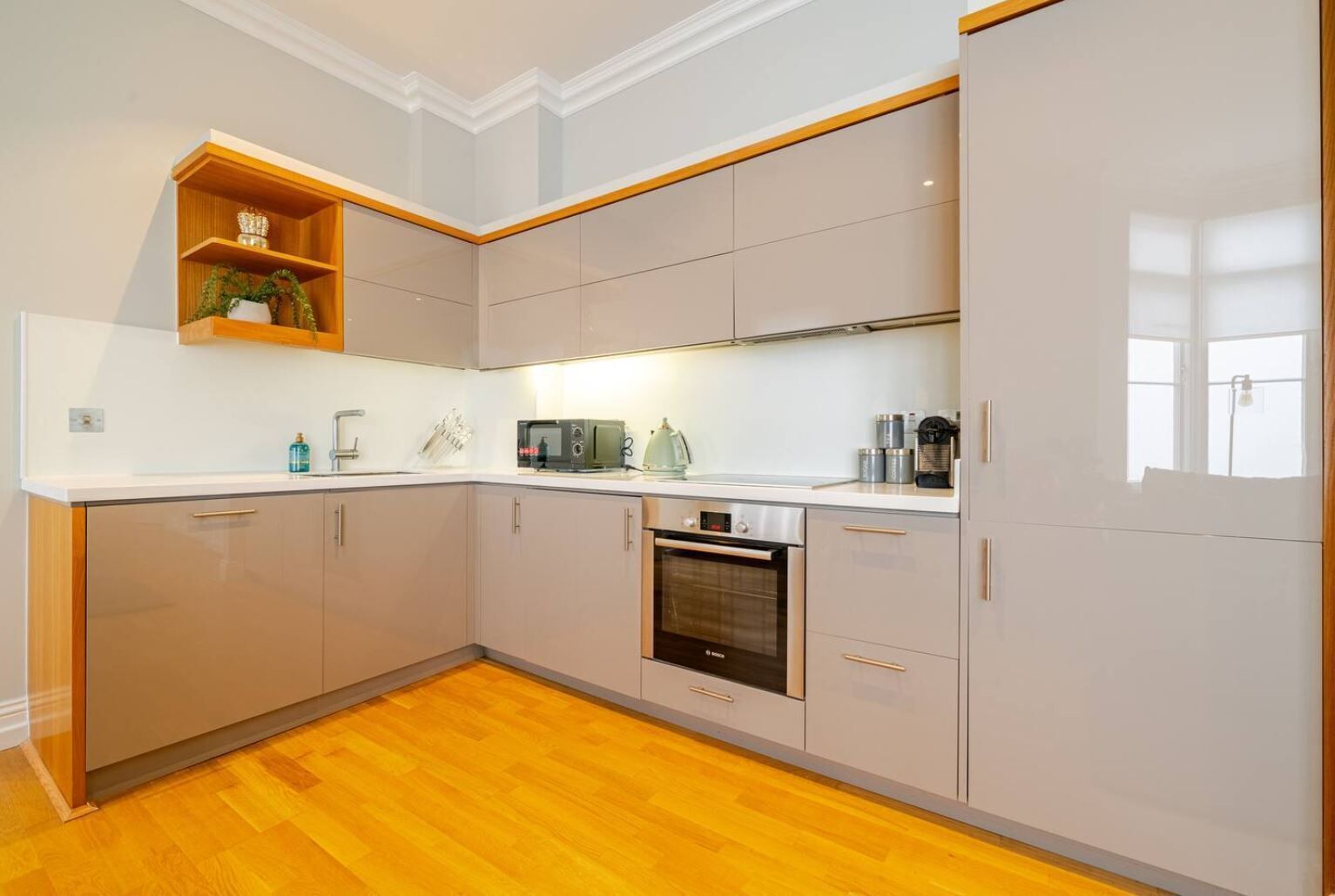 A modern kitchen with a built-in oven, microwave, and a wooden shelf with decorative items.