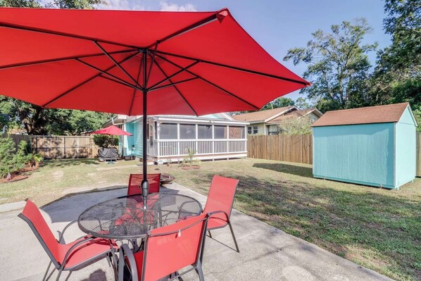 A backyard patio with a round table, red chairs, and a large red umbrella.