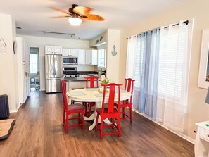 A modern kitchen with white cabinets, a stainless steel refrigerator, and a dining area with a round table and red chairs.