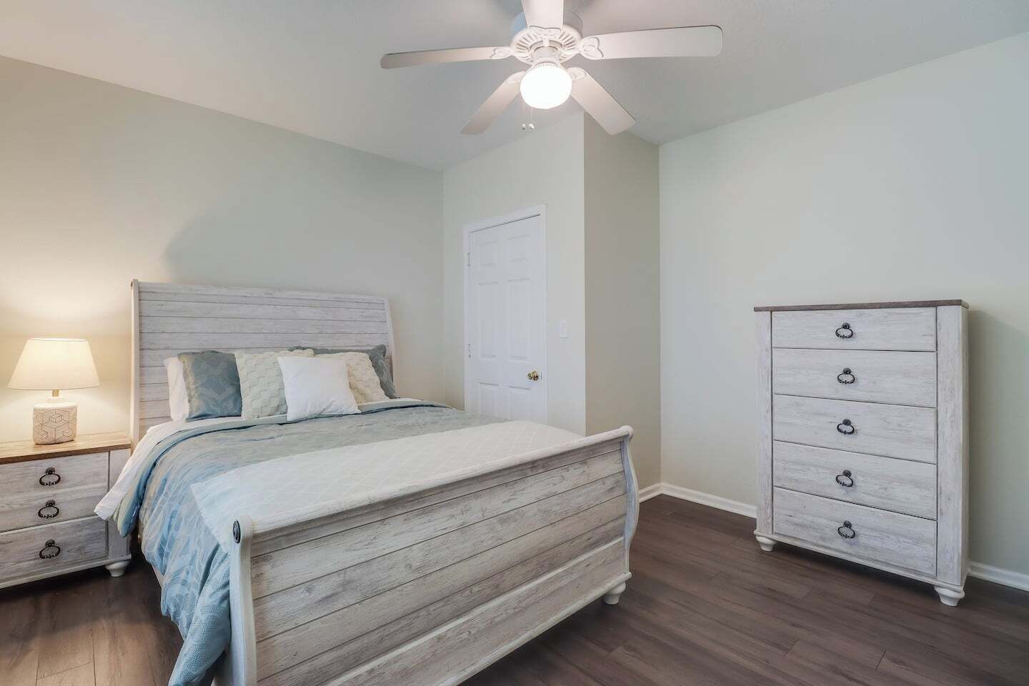 Une chambre à coucher comprenant un lit, une commode, une table de chevet et un ventilateur de plafond.