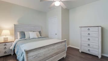 Une chambre à coucher comprenant un lit, une commode, une table de chevet et un ventilateur de plafond.