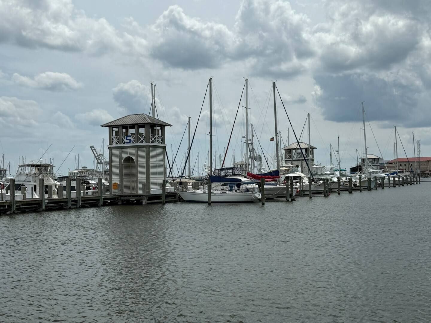 A marina with multiple boats docked, a small tower structure, and a cloudy sky.