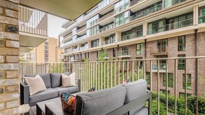A balcony with grey sofas and a table, overlooking a multi-story building with balconies. - The London Dock HQ - 3 Beds for 6 Guests with AC (London)
