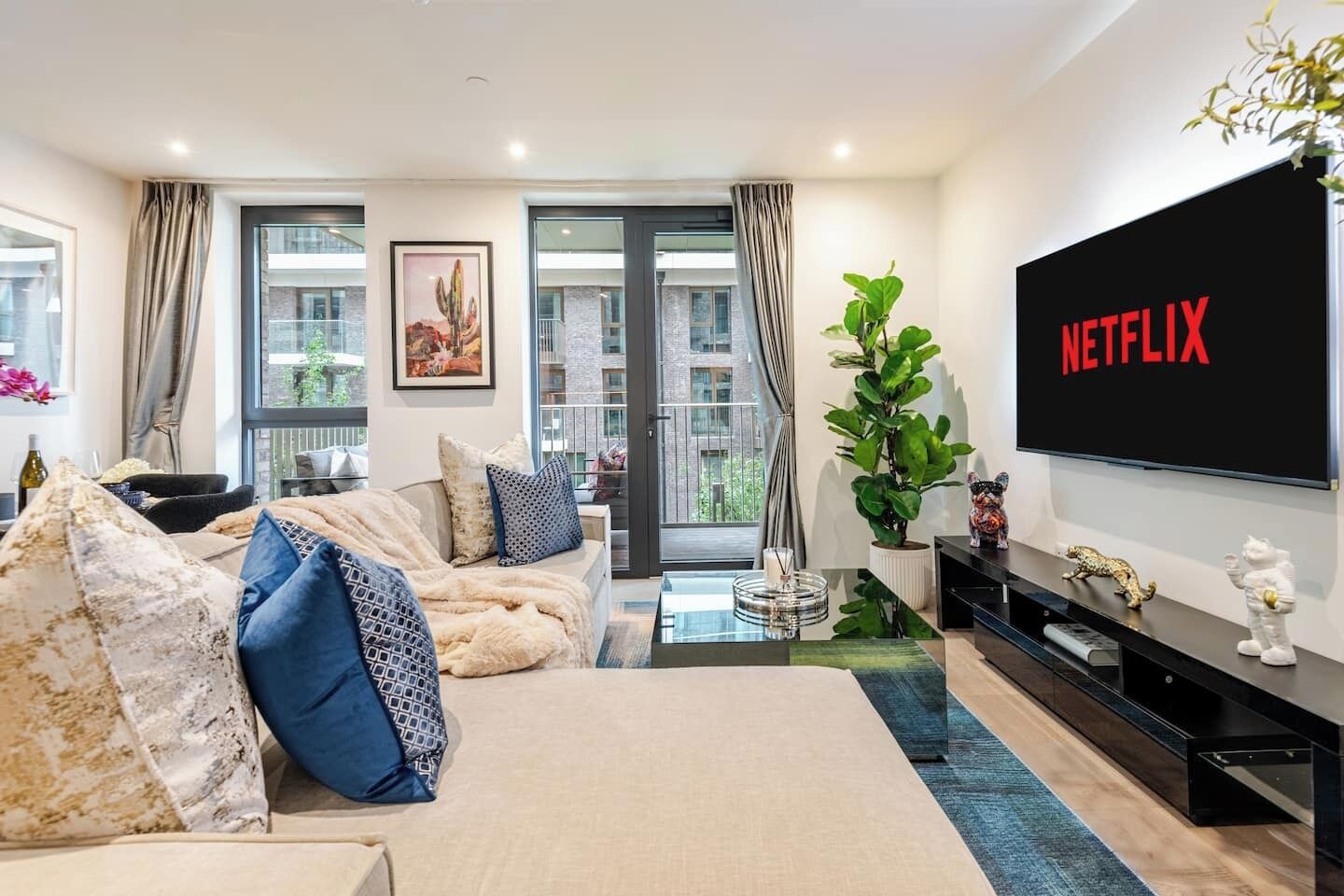 A modern living room with a large flat-screen TV, a sofa, a coffee table, and a potted plant.