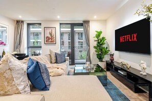 A modern living room with a large flat-screen TV, a sofa, a coffee table, and a potted plant.