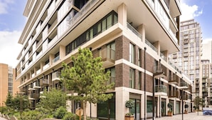 Un edificio a più piani con un design architettonico moderno, caratterizzato da balconi, ampie finestre e un cortile interno curato con alberi e fioriere.