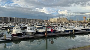 A marina with numerous boats docked, a waterfront promenade, and a backdrop of buildings and a water tower.
