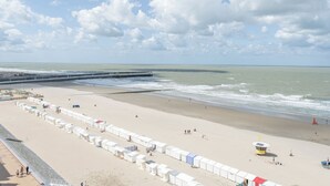 A beach with a row of white tents, a lifeguard tower, and a pier extending into the sea.