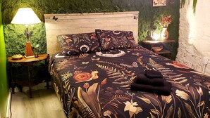 Un dormitorio con pared cubierta de musgo verde, cabecero de madera, colcha estampada con motivos florales y lámpara colgante.