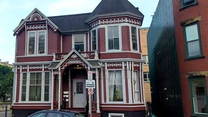 Una casa de estilo victoriano con un amplio ventanal saliente, un porche delantero y un coche negro estacionado en la calle.