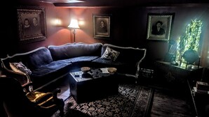 Una habitación oscura con un sofá de cuero, una mesa con cuencos y retratos enmarcados en la pared.