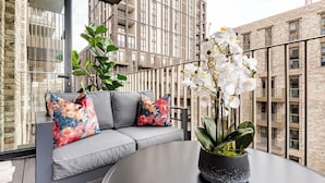 Un espace extérieur moderne, aménagé avec un canapé gris, des coussins aux motifs floraux colorés et un pot d’orchidée.