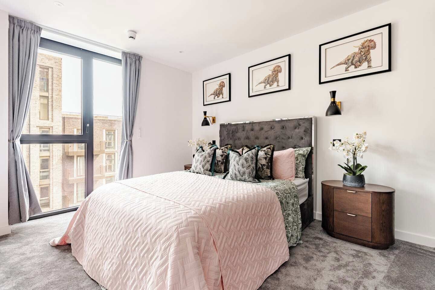 A bedroom with a large bed, a nightstand, a window with curtains, and framed artwork on the wall.