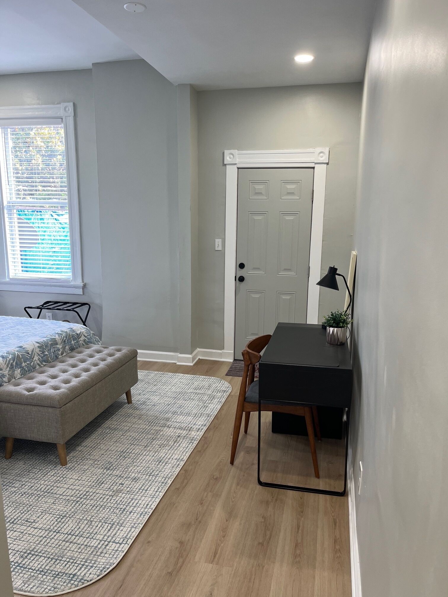A small, well-lit room with a bed, a desk, and a chair.