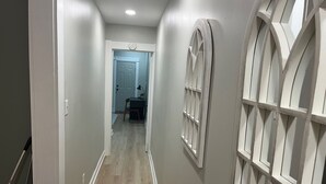 A hallway with a wooden floor, white walls, and a door at the end.
