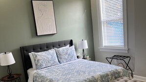 A bedroom with a bed, bedside lamps, a bench, a window with blinds, and a wall-mounted picture.
