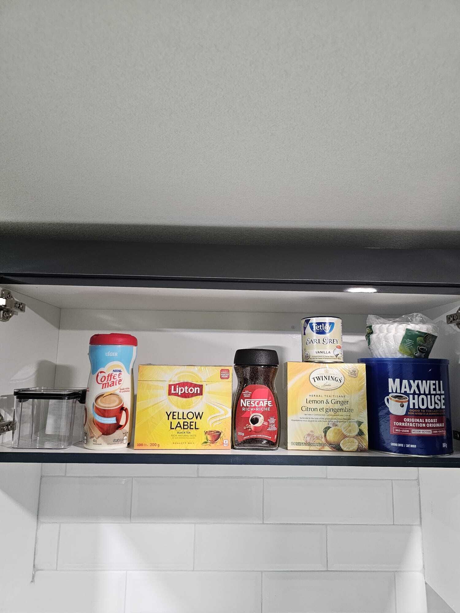 A kitchen shelf with various coffee products including a coffee maker, Lipton tea, Nescafe, Twinings tea, and Maxwell House coffee.