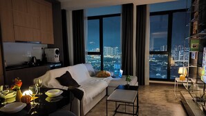 Ein modernes Wohnzimmer mit einer Couch, einem Esstisch und Blick auf die Stadt durch große Fenster.