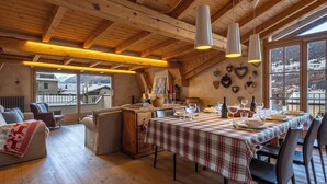 A cozy dining area with a wooden ceiling, a table set for four, and a view of the mountains through large windows.