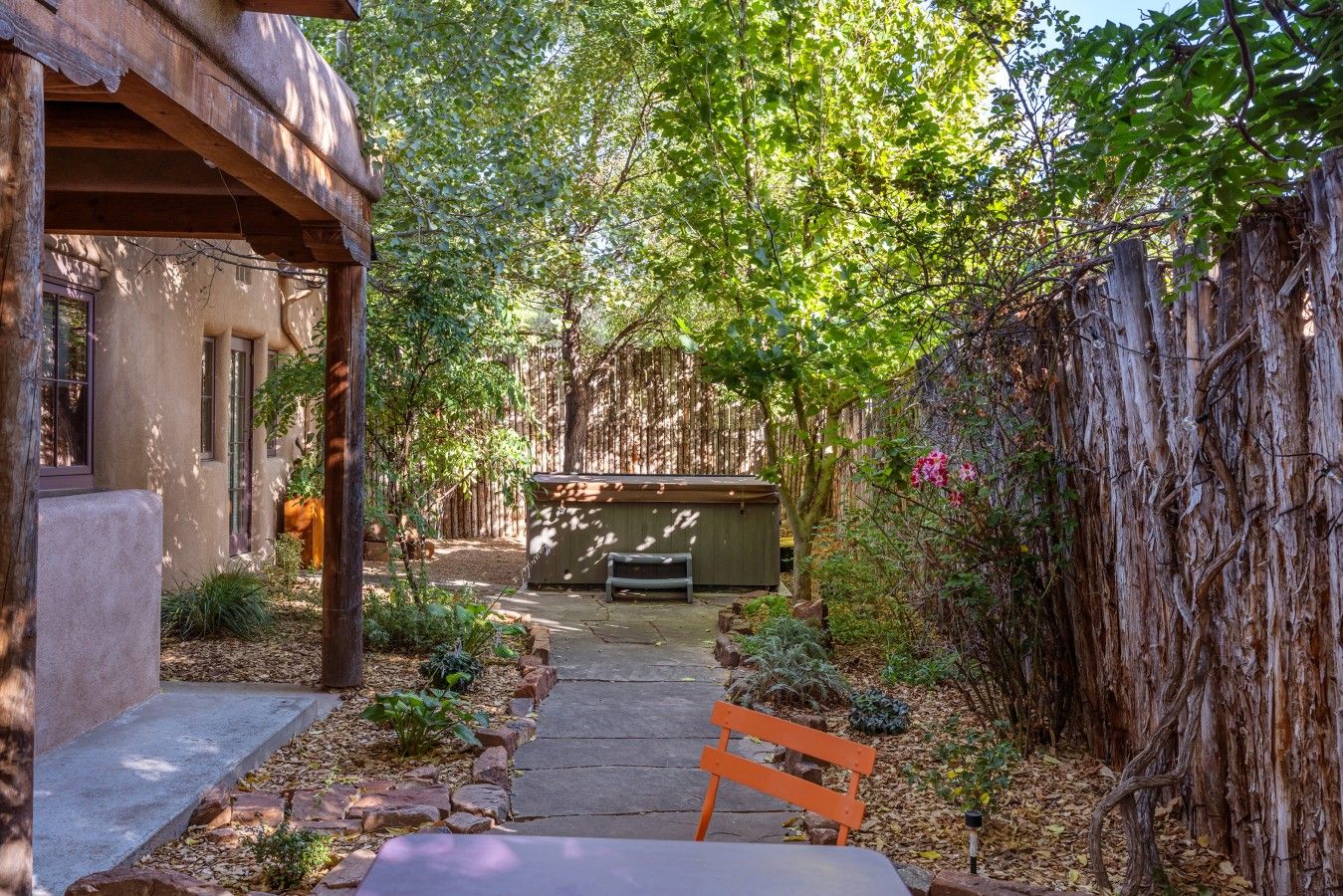 Un sendero de jardín que lleva a una estructura de madera con un banco, rodeado de árboles y una valla de madera.