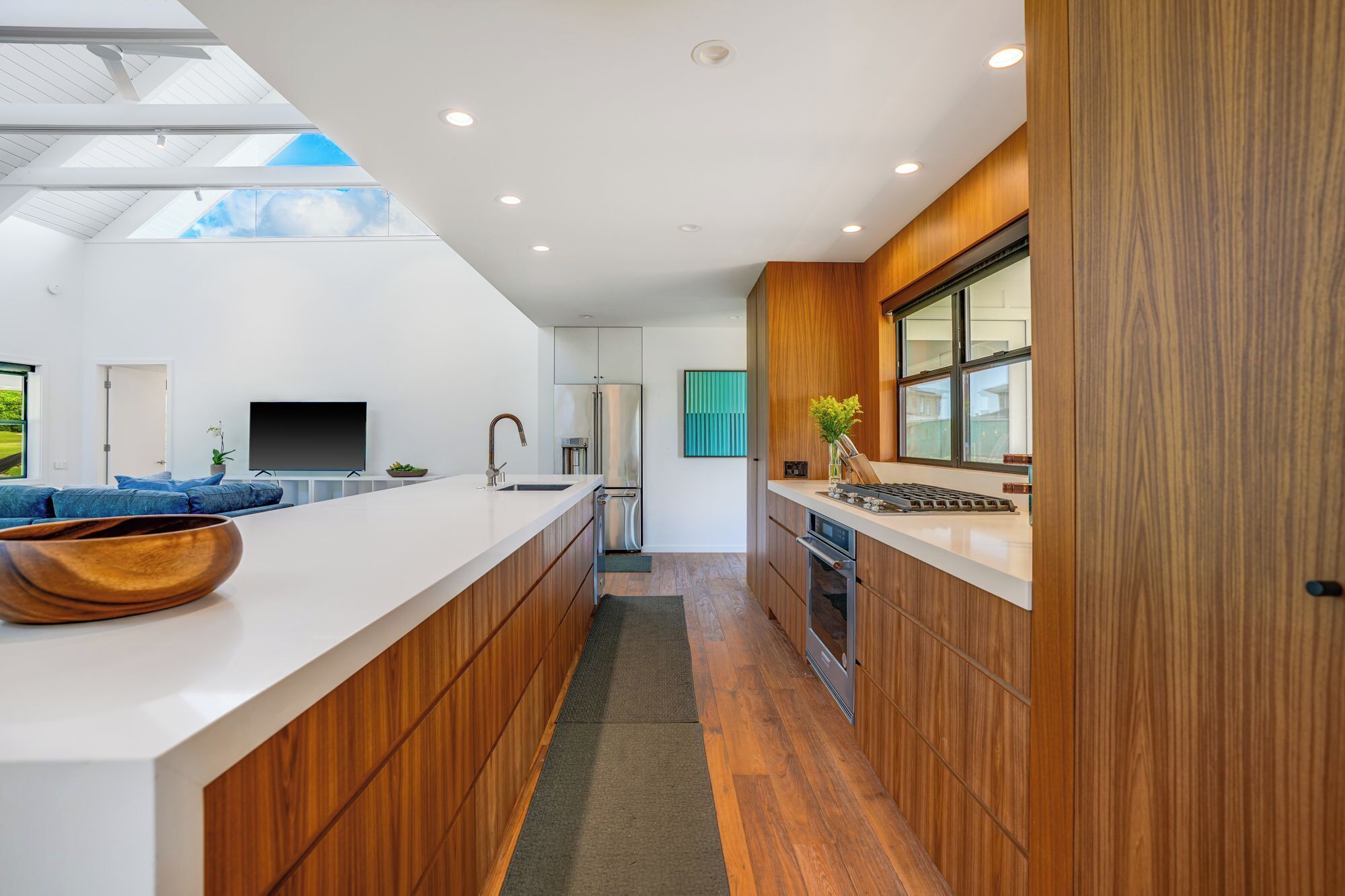 A modern kitchen with a large island, wooden cabinets, and a view of the outdoors.
