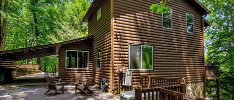 A log cabin with a porch, outdoor seating, and a view of the surrounding forest.