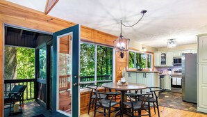 A modern kitchen with wooden cabinets, a dining area with a round table and chairs, and large windows offering a view of the outdoors.