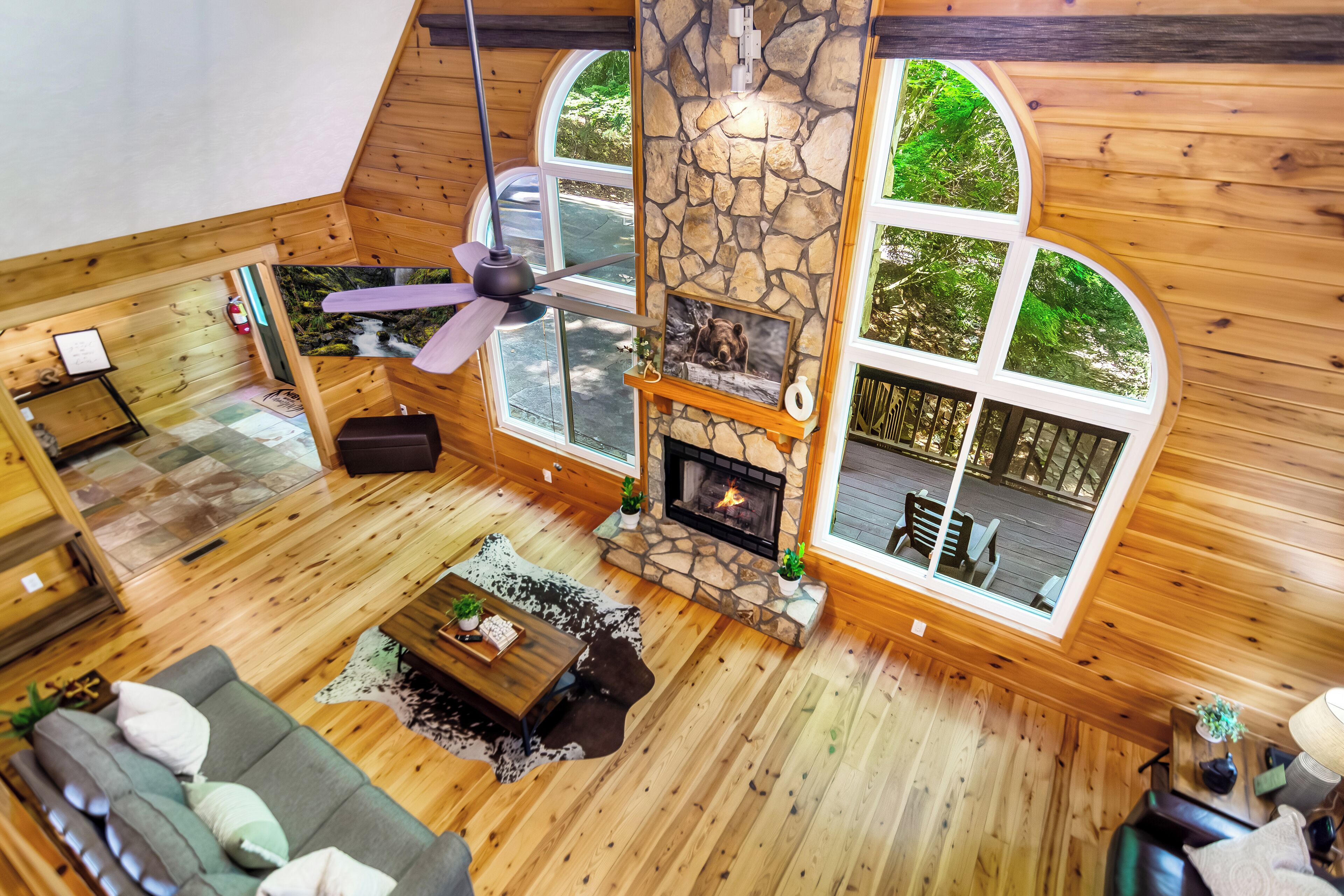 Amplia habitación estilo loft con chimenea de piedra, pisos de madera y grandes ventanas que ofrecen vistas al exterior.