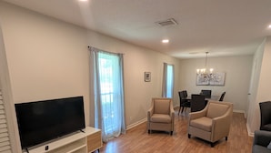 A spacious living room with a flat-screen TV, two beige armchairs, a gray sofa, and a dining table with chairs. - Forget your worries in this spacious and serene space. (Monroe)