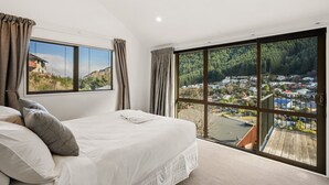 A bedroom with a large bed, two windows, and a view of a town and forest.