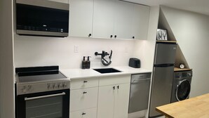 A modern kitchen with white cabinets, a built-in oven, a sink, a toaster, and a washing machine.